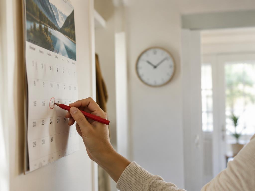 Hand marking a date on a wall calendar at home